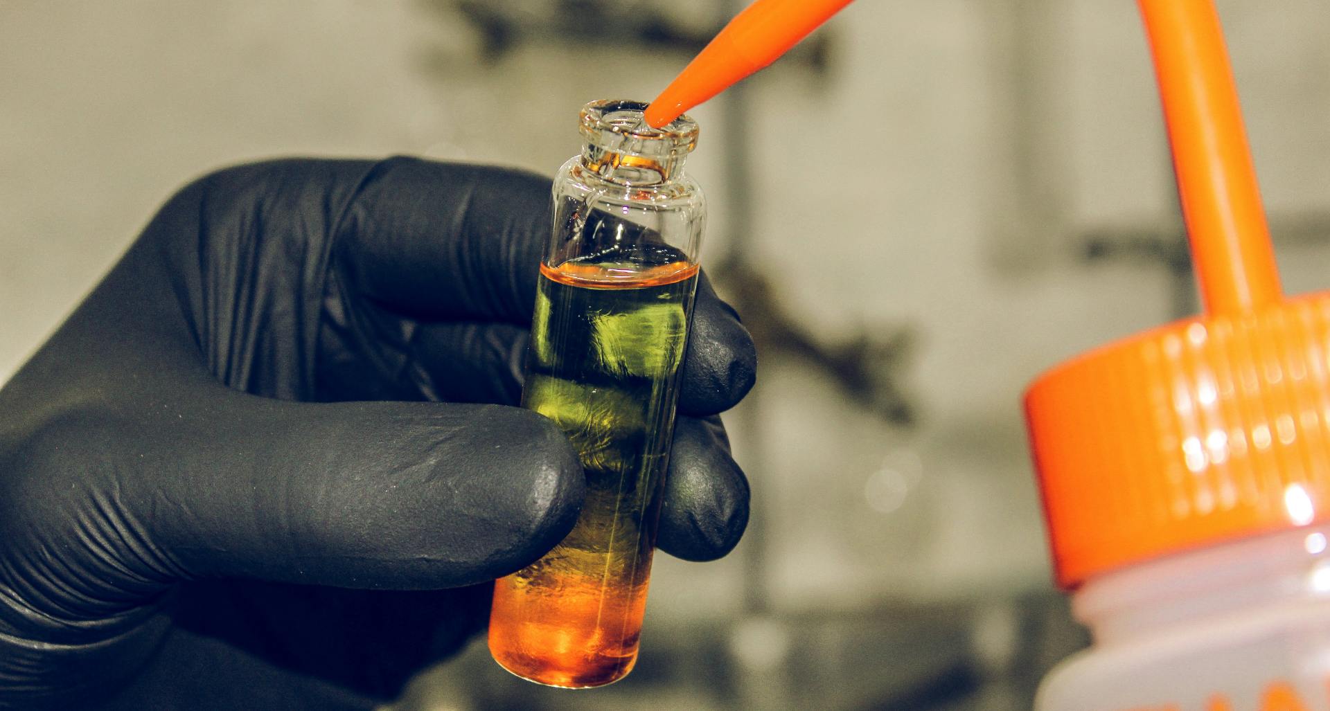 Gloved hand holding a beaker of clear chemical solution